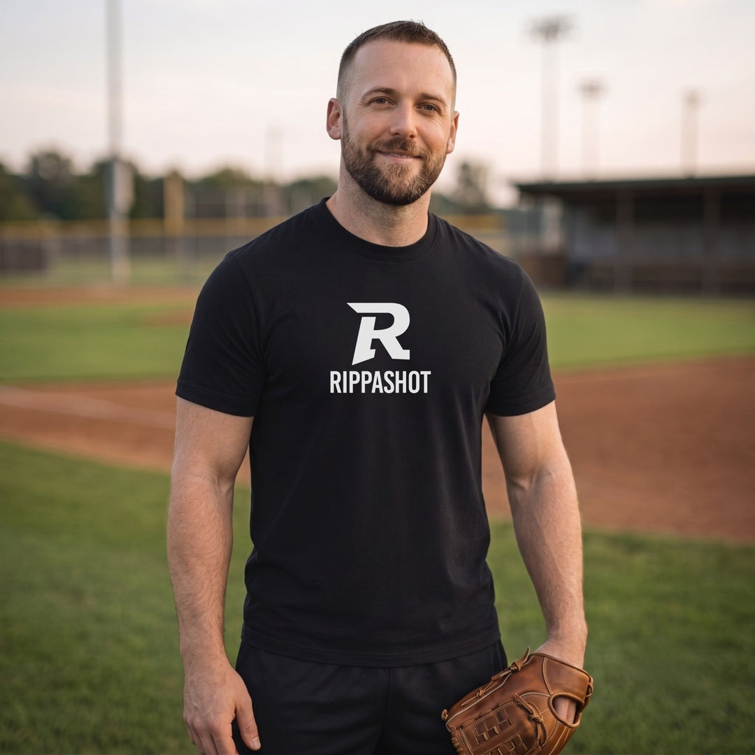 A man standing on a baseball field wearing a black short-sleeve t-shirt with a white &