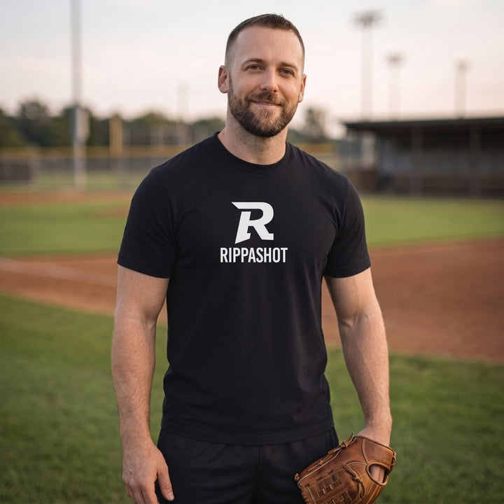 A man standing on a baseball field wearing a black short-sleeve t-shirt with a white &