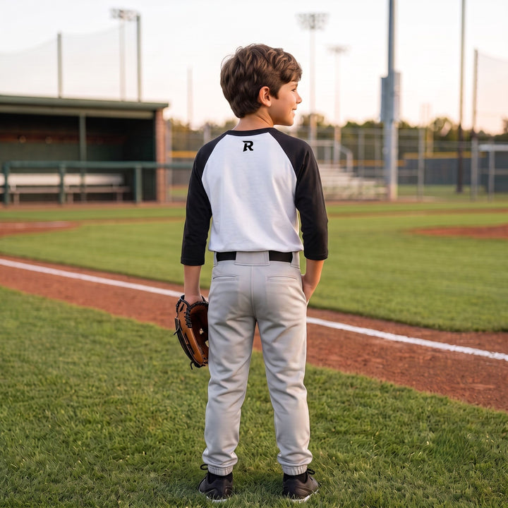 Youth baseball player wearing RIPPASHOT raglan tee with R on back neck and glove on his hand at baseball field