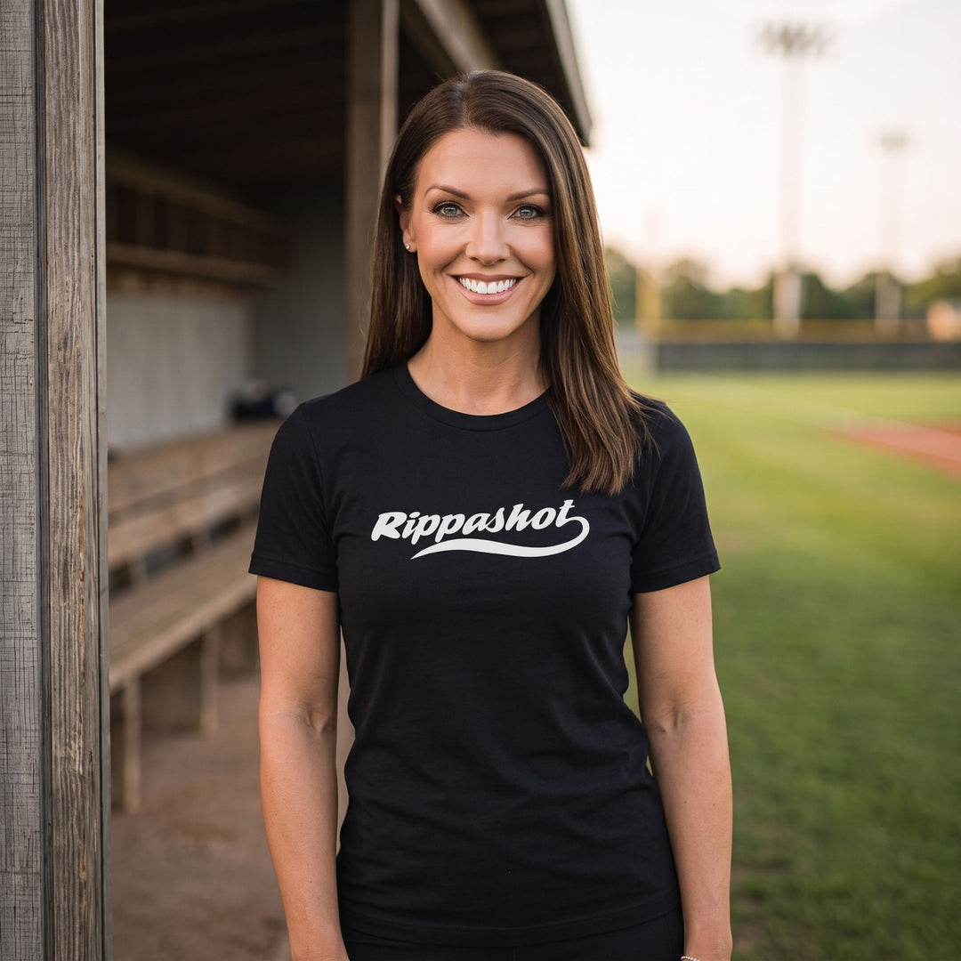 A woman standing on a baseball field wearing a black crewneck t-shirt with the words &