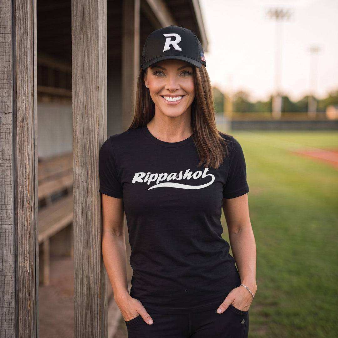 A woman stands on a baseball field wearing a black t-shirt with &